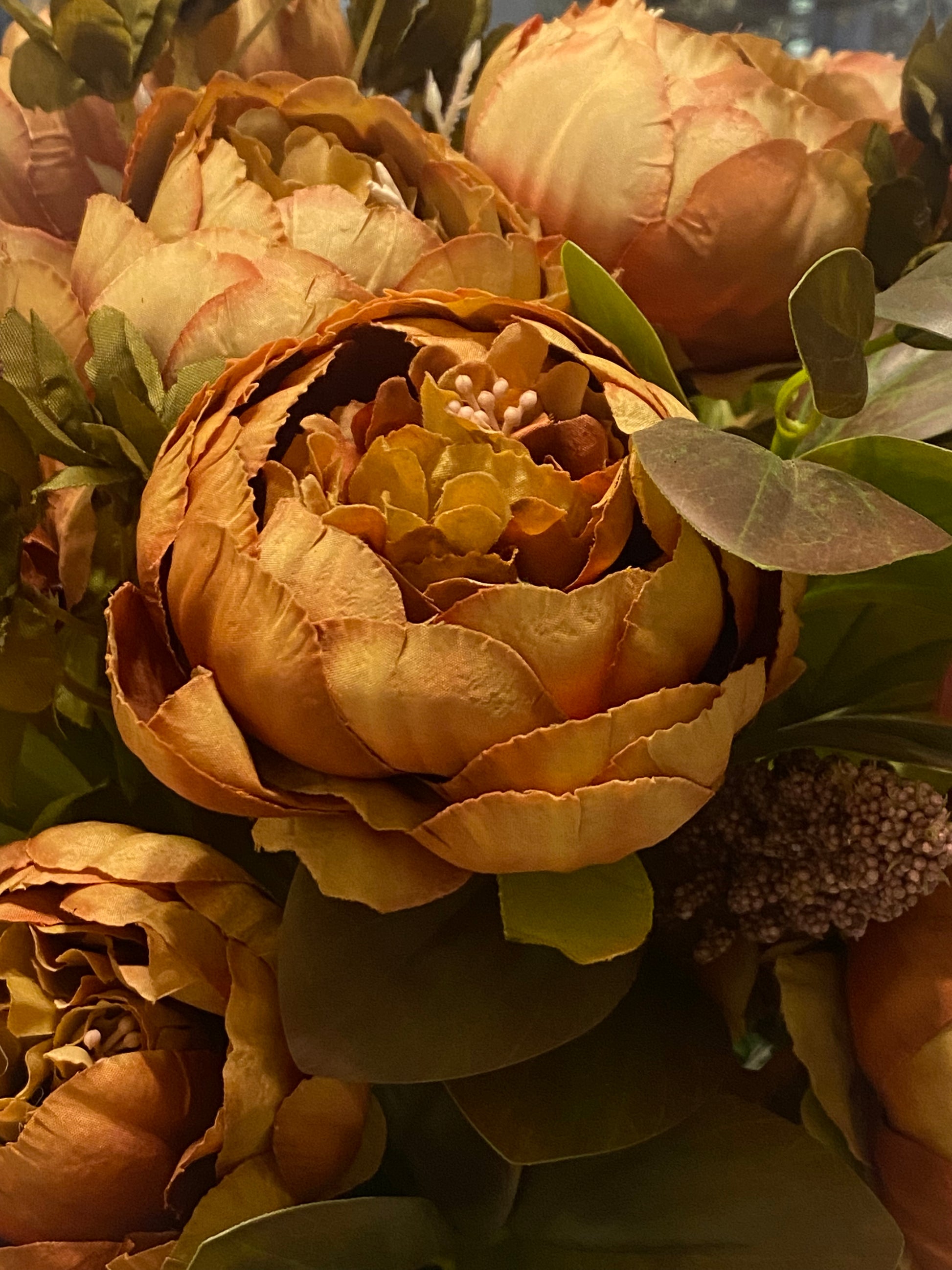 Close-up of a bouquet of peony flowers with autumnal tones and green leaves.