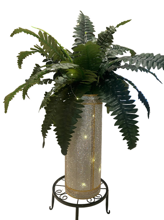 Silver crystal rhinestone vase trimmed with gold and fern greenery on a plant stand with string lights